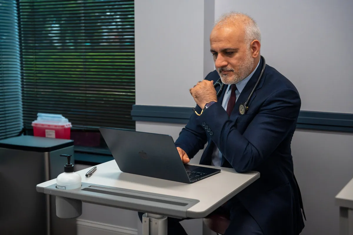 Dr. Suresh Malik reviewing a chart on a laptop in a Quality Primary Care Associates exam room