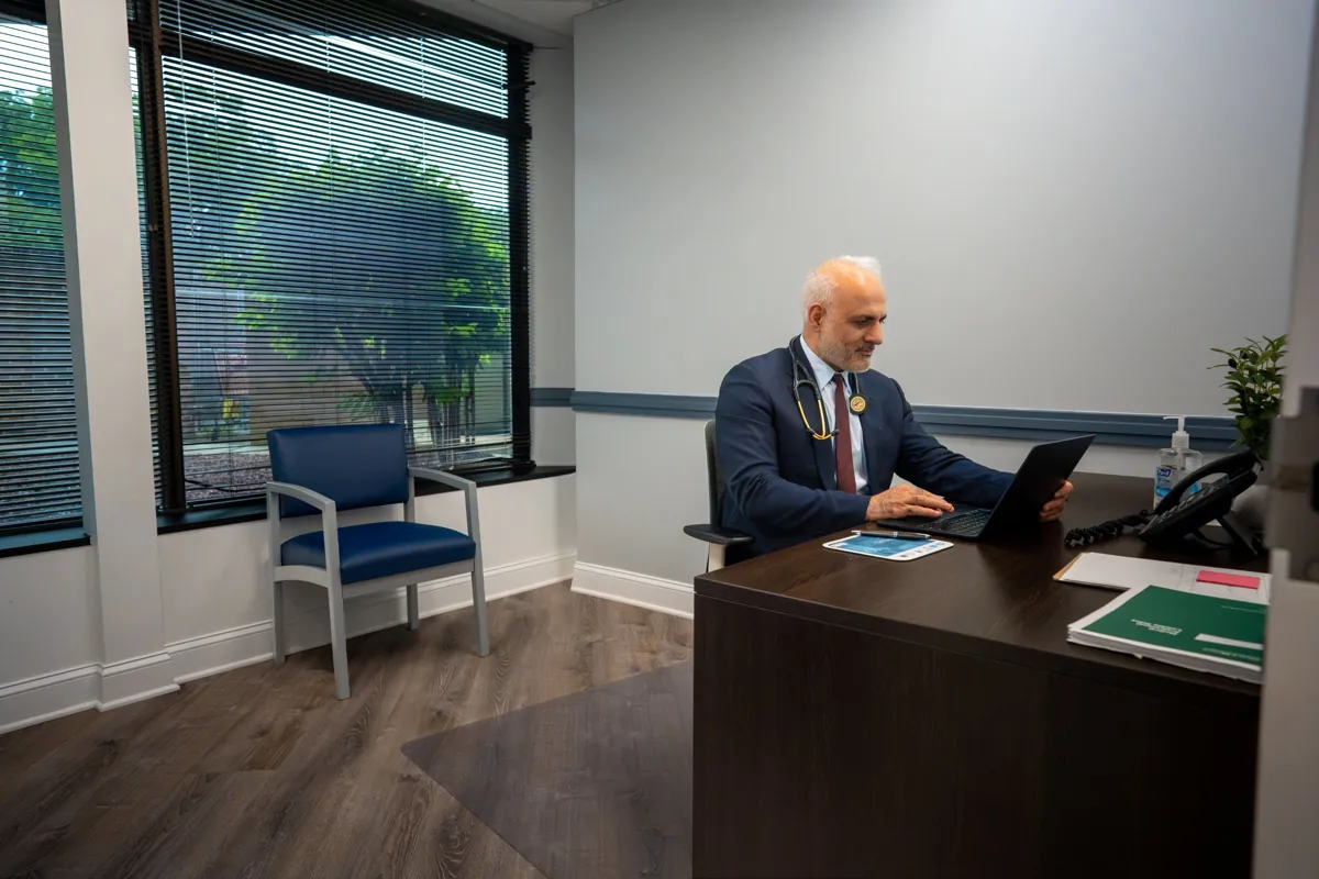 Dr. Suresh Malik working at a desk in a consultation office at Quality Primary Care Associates