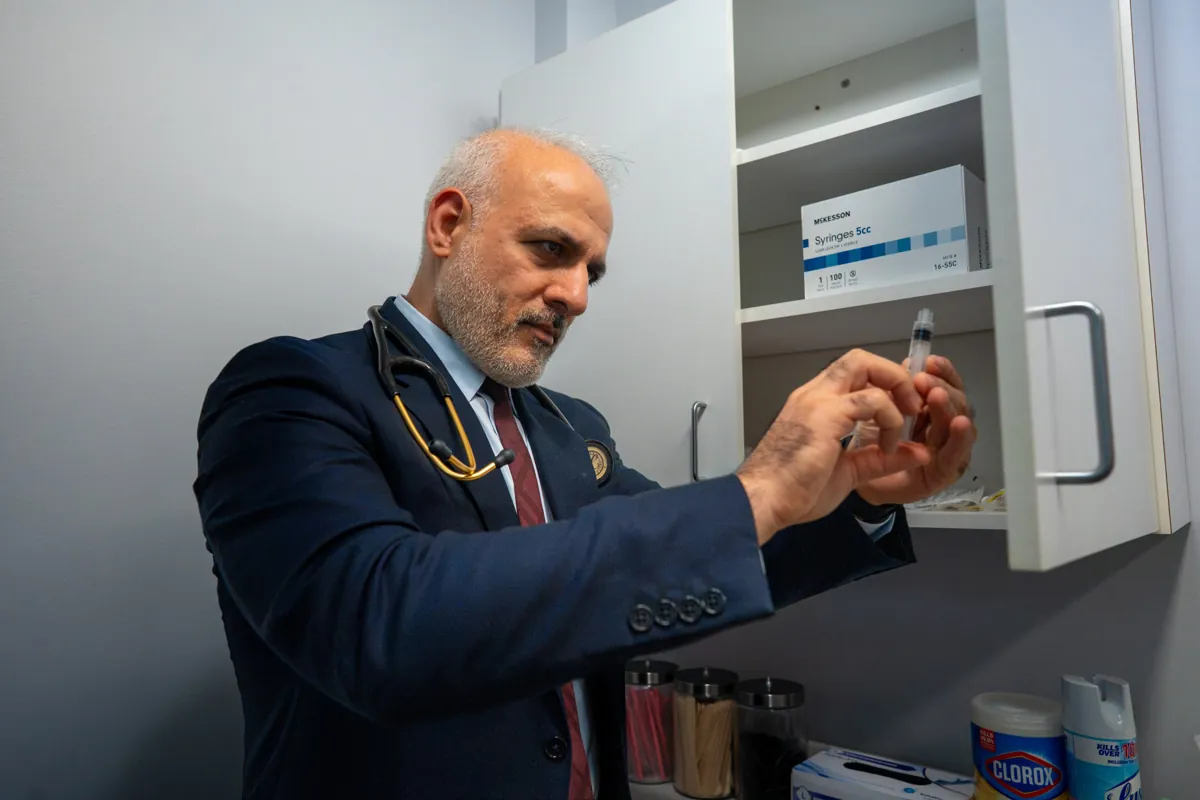 Dr. Suresh Malik checking a syringe at a supply cabinet in a Quality Primary Care Associates exam room