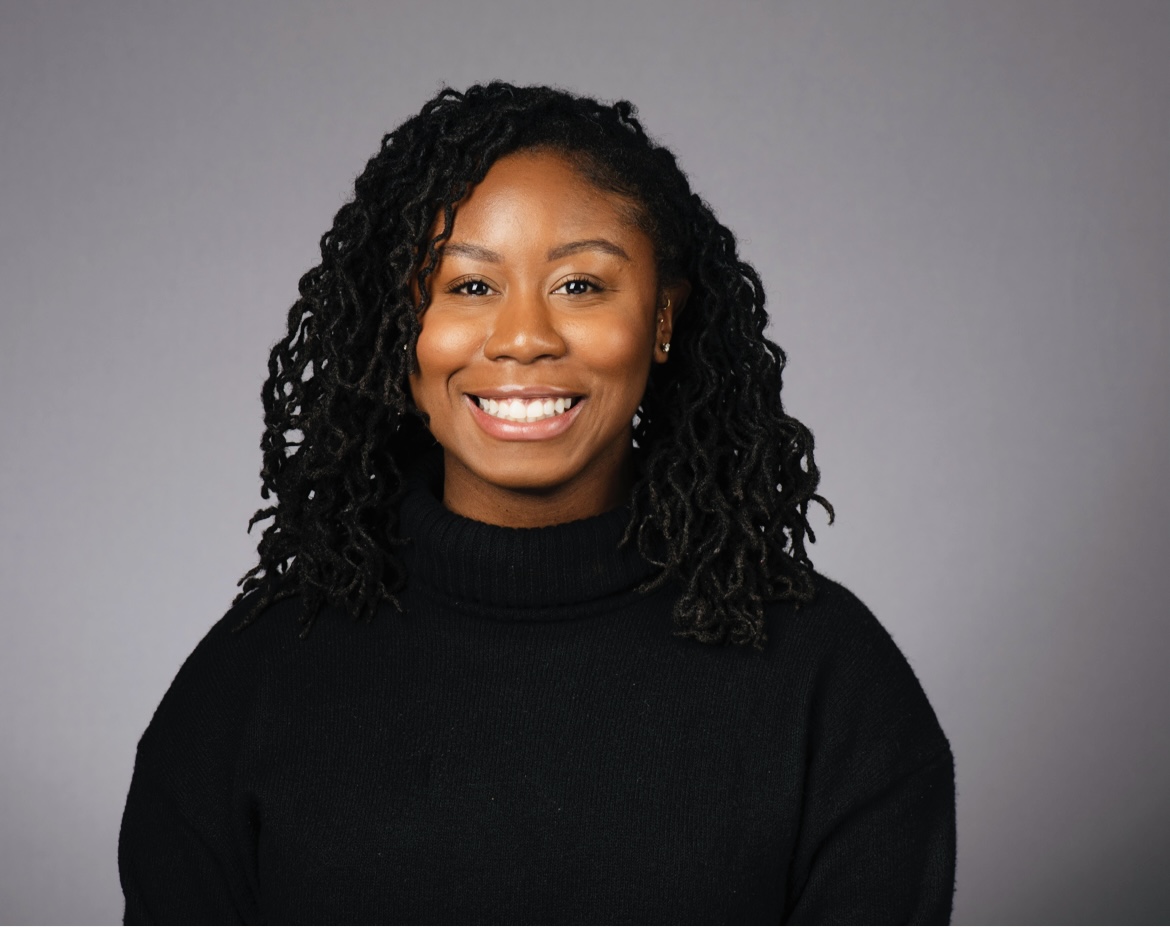 Person smiling with black sweater background gray.