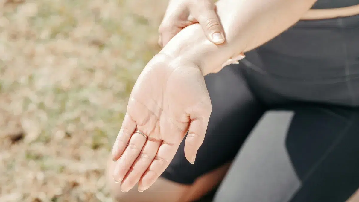 Person holding wrist, outdoor setting.